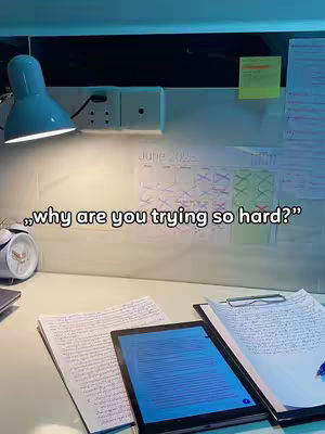 A well-lit workspace featuring a desk with papers, a tablet displaying a blue screen, and a calendar. The scene includes a desk lamp, an alarm clock, a power outlet, and a post-it note.