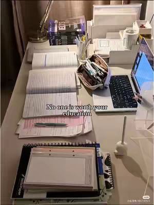 A top-down shot of a desk covered in study materials, including open books, notebooks, pens, a laptop, and a desk lamp. The image is well-lit, with a neutral color palette, and the text overlayed says, 'No one is worth your education.'