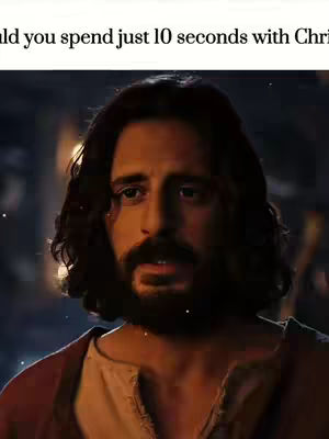 The image is a medium shot featuring a man with long, dark hair and a prominent beard, positioned from the chest up. He is wearing a long-sleeved, earth-toned garment with a reddish-brown outer layer. His expression is one of thoughtful reflection, with his eyes slightly downcast, suggesting contemplation. The background is blurred, but hints at a dimly lit interior, maybe a nighttime scene. Light appears to be concentrated on his face, highlighting his features. Subtle light particles are scattered throughout the image, adding a ethereal quality