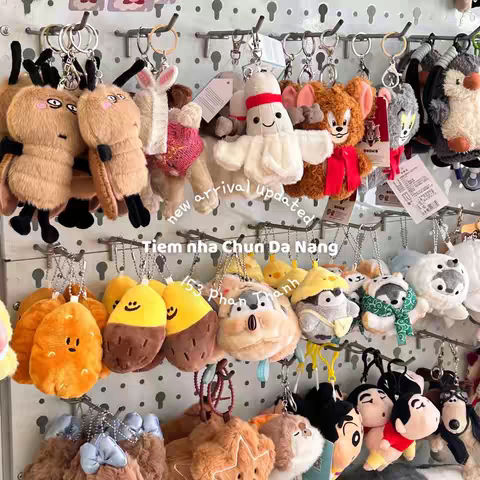 A display of assorted plush keychains hanging on metal hooks arranged against a white background. The keychains are colorful and feature different animal designs like bears, bunnies, and fruit.