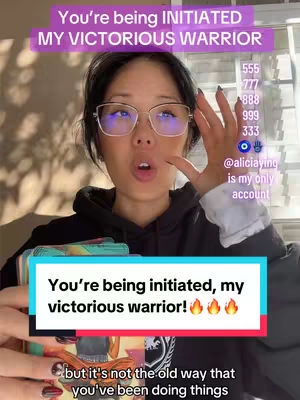 The cover features a woman with glasses looking at the camera with an open mouth. Overlay text saying "You're being INITIATED MY VICTORIOUS WARRIOR" is at the top. Additional text and numbers are displayed on the right side. At the bottom, a text box reads "You're being initiated, my victorious warrior!" along with flame emojis. The background is a blurred indoor setting.