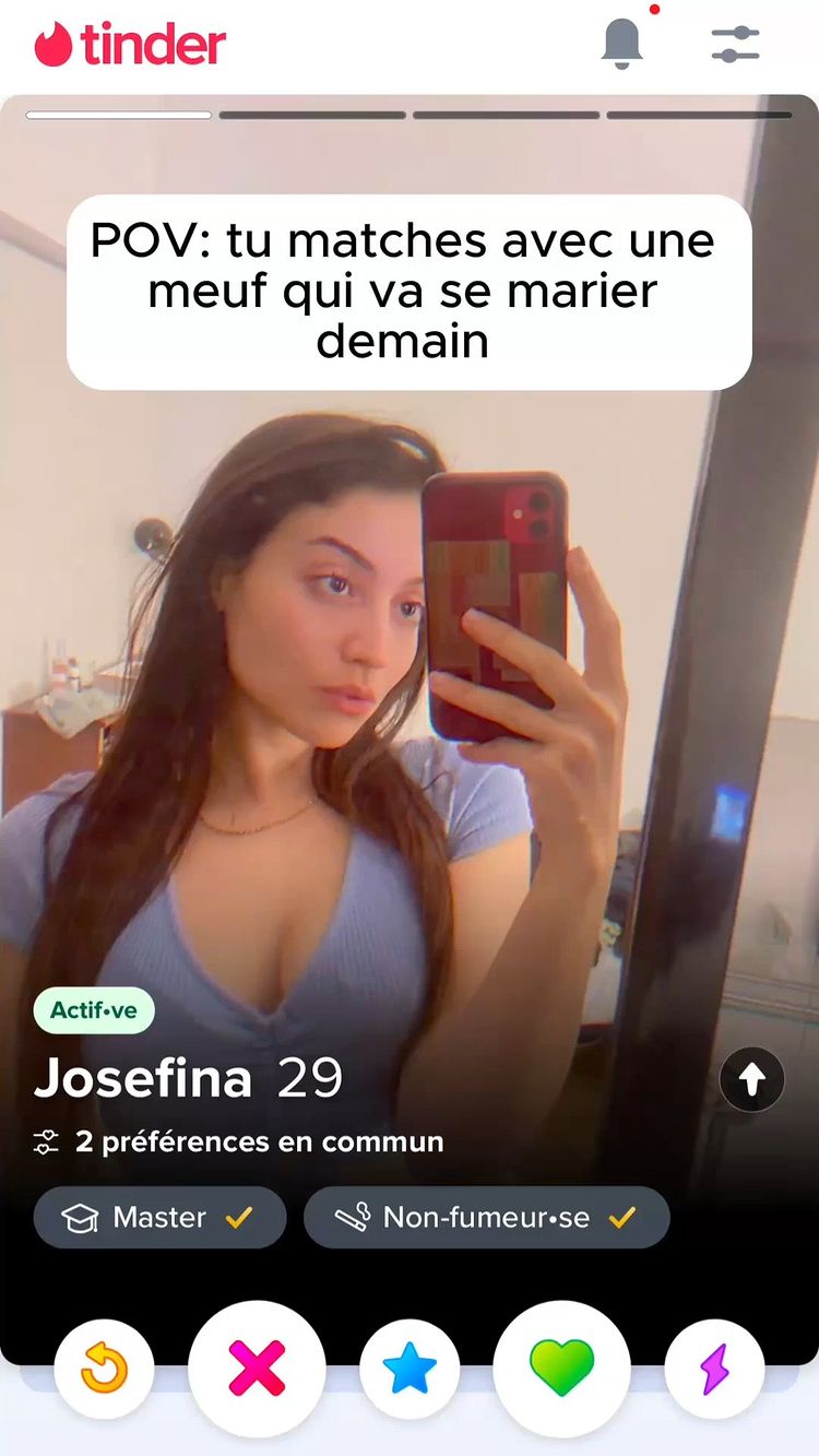 A Tinder app interface is displayed on a phone. A woman is taking a selfie with the phone. The woman has long brown hair and is looking into the camera. A text bubble at the top of the phone screen says, "POV: tu matches avec une meuf qui va se marier demain." Below the woman, there are app buttons visible: a red 'X', a blue star, and a green heart.