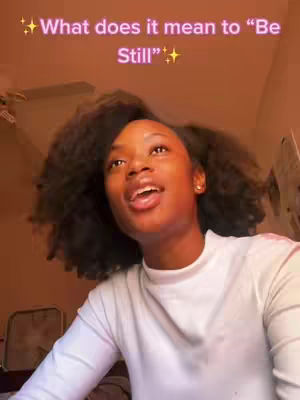 A young woman with dark, curly hair is centered in the frame, her face turned slightly to the side with her mouth open as if speaking. She is wearing a white long-sleeved shirt. Above her, overlaid on the image, is the question 'What does it mean to "Be Still"?'. The background is a warm, muted orange.