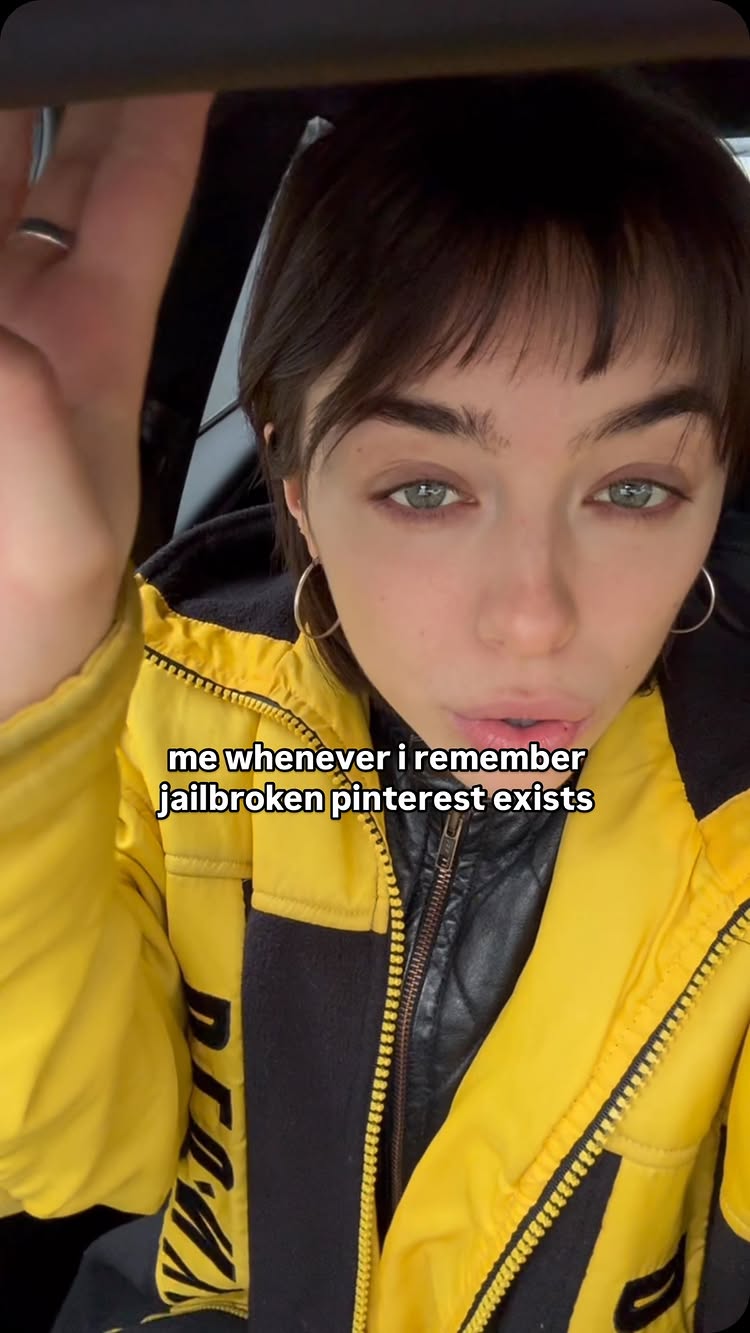A selfie-style shot featuring a woman in the driver's seat of a vehicle. She has dark hair, green eyes, and is wearing a yellow jacket with black accents. The text overlay on the image says "me whenever i remember jailbroken pinterest exists". The background is blurred, likely showing the interior of a car.