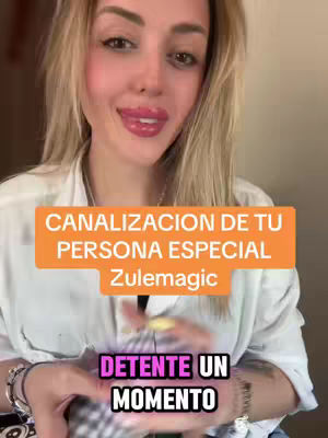 A woman with long blonde hair is centered in the frame, directly facing the camera with a gentle smile. She has full lips and is wearing a white button-up shirt. Overlaid on the image are two text boxes. The first, in a bright orange rectangle, reads 'CANALIZACION DE TU PERSONA ESPECIAL Zulemagic.' Below, in white text on a purple rectangle, it reads 'DETENTE UN MOMENTO'. The background is blurred, suggesting an interior setting.