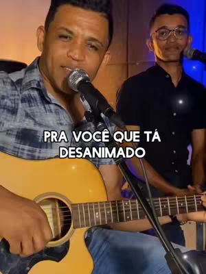 The cover image features two men, one playing an acoustic guitar and singing into a microphone, while the other stands beside him. The foreground man is in a plaid shirt and jeans, with a serious expression. The background man, wearing glasses and a dark shirt, appears to be providing backing support. Text overlayed in the image reads: 'PRA VOCÊ QUE TÁ DESANIMADO'. The lighting is warm, and the overall composition suggests a musical performance.