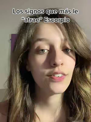 A young woman with long brown hair and fair skin is centered in the frame, looking directly at the camera, her lips slightly parted as if speaking. A text overlay at the top reads, 'Los signos que más le atrae Escorpio,' in a bold, white font against a dark backdrop. The lighting is soft and even, illuminating the woman's face and hair, creating a focused composition.
