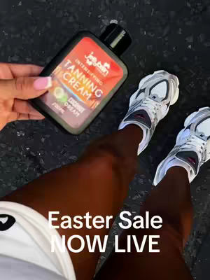 A low-angle shot shows a person's legs with dark skin tone, wearing white sneakers. The person holds a bottle of tanning cream with a black cap and orange label. The background is a dark surface. Text overlayed at the bottom says, 'Easter Sale NOW LIVE.'