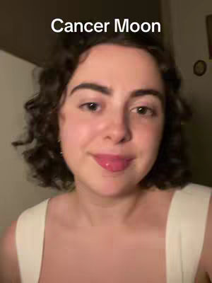 A selfie-style shot featuring a young woman with dark, curly hair and fair skin. The top of the image displays text overlay that reads: Cancer Moon.