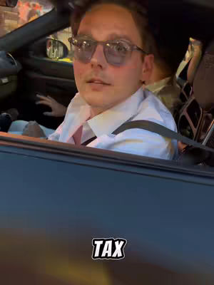 A man wearing sunglasses is in the driver's seat of a car. The foreground is the car's dashboard, and the hook 'TAX' is displayed at the bottom.