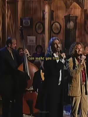 The image shows a group of men singing on a stage with musical instruments, including a double bass. The background includes wooden paneling, old clocks, and pictures.