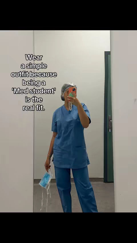 A mirror selfie shows a person in blue scrubs, a surgical cap, and holding a mask. Text overlays the image. The person is self-reflecting, with a simple white wall background.