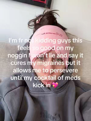 A selfie-style video shows a person with dark hair pulled back, wearing a gray hoodie and a pink migraine relief cap. Text overlays on the image.
