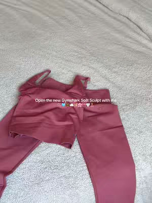 The cover image shows a set of Gymshark activewear, a top and leggings, in a dusty rose color. The clothing items are laid out on a white, textured surface, possibly a bed or a blanket. Text is overlaid on the image.
