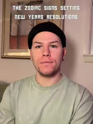 A man with short hair and a black beanie poses with a neutral expression in front of an abstract painting. Text overlays the top portion of the image.