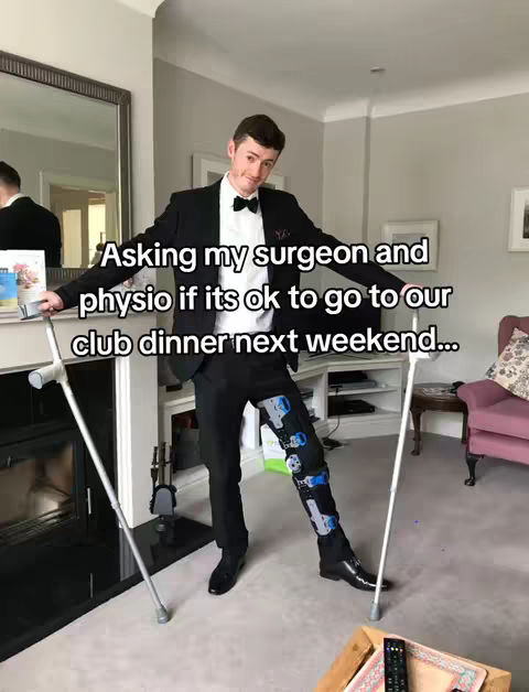 A man in a black suit and bow tie stands with crutches and a leg brace in a well-lit living room. Text overlays ask if it is okay to attend a club dinner.