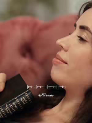 A woman with brown hair and closed eyes is resting, holding a black Bible. The background is blurred, with a hint of pink fabric. A visual sound wave and the username @Winnie are overlaid at the bottom.