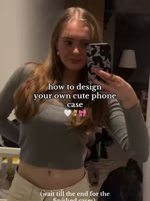 A selfie-style shot featuring a young woman holding up a phone case. The image is warm-toned, with the woman in a long-sleeved gray top and light-colored pants. Text overlays include promotional copy and design instructions. The background appears to be a domestic setting, with a mirror reflecting elements of the room, including personal items and a lamp.