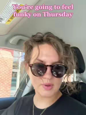 A woman with sunglasses is sitting in car, with a pink text overlay. The car has a sun visor, and the setting seems to be a sunny day. The woman is looking at the camera, and there is an outside background, possibly a drive-through window.