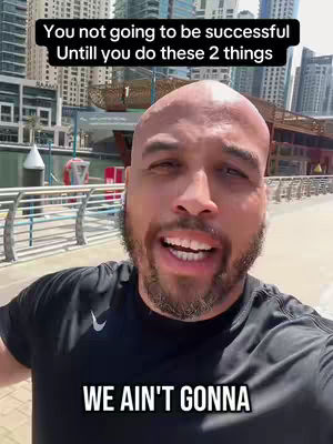 An outdoor selfie featuring a man with a shaved head and beard, framed from the chest up. He's in front of a cityscape with reflective buildings and a body of water. The man is smiling with his mouth open, seemingly mid-sentence. Text overlays the image in bold white fonts.