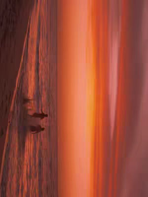 The image shows a vibrant sunset or sunrise with warm tones. Two silhouetted figures are seen running towards the left side of the frame, suggesting a couple. The colors in the sky transition from orange to pink.
