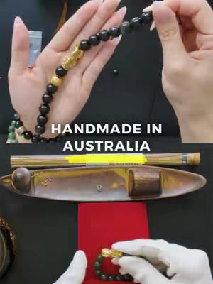 The image shows a top-down view of a table setup with a bracelet being displayed. Two hands, one wearing a white glove, are handling the bracelet. Parts of the bracelet are visible, showing black beads and a gold-colored dragon charm. Other visible objects include a red cloth, what seems to be an incense holder with multiple incense, and a tray containing the incense sticks. The text overlayed reads 'HANDMADE IN AUSTRALIA'.