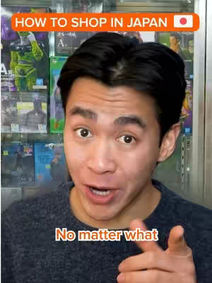 A man with dark hair and a grey sweater looks directly at the camera with an open mouth, seemingly speaking. Above him is an orange bar with the words 'HOW TO SHOP IN JAPAN' and a Japanese flag on the right-hand side. Behind him are displays of what appear to be various merchandise items.