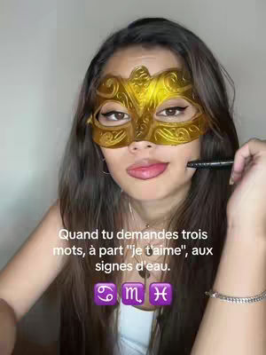 A woman wearing a gold masquerade mask is shown, with her tongue slightly out. Text is overlaid on the image, along with three zodiac symbols.