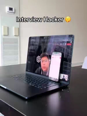 A laptop sits on a table, displaying a video call and a smartphone. The laptop screen features a person, while the phone shows a white screen with a possible app interface. Above the laptop is a text overlay.