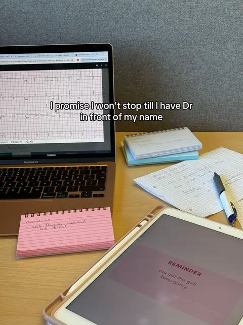 A desk setup with a laptop, tablet, notebooks, and flashcards. The laptop displays an EKG. A pink flashcard is visible with handwritten notes. The tablet shows a reminder 'you got this girl! keep going'.