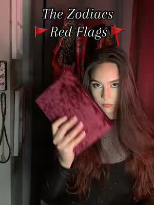 The cover image shows a woman in a dimly lit setting, holding a red velvet book, and looking directly at the camera with a serious expression. Text overlayed on the image reads 'The Zodiacs Red Flags', marked with flag icons.