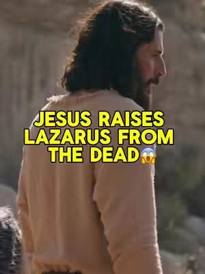 The image shows a man with long hair and a beard, dressed in light-colored clothing, viewed from the back and right side. A text overlay in a yellow box reads, "JESUS RAISES LAZARUS FROM THE DEAD". The overall composition suggests a scene from a historical or religious context, possibly a movie or a depiction of a biblical event.