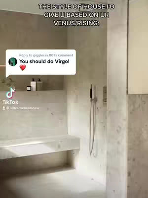 The image shows a modern, minimalist bathroom scene. The primary focus is on a shower area with light-colored stone or tile walls. A built-in bench is present on the side. A comment bubble overlays, containing the text "You should do Virgo!" with a heart emoji, suggesting the video's content will be related to this astrological sign. The overall composition is clean and the lighting is bright, giving an impression of spaciousness and modern design.