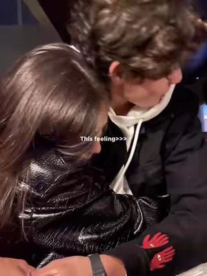 A close-up shot of a couple embracing, with the woman's head resting on the man's shoulder. The image is slightly blurred, suggesting a focus on emotion. A text overlay reads 'This feeling>>>'.