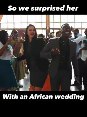 The cover image shows a joyful couple walking towards the viewer in a group of wedding guests. The text overlay "So we surprised her" and "With an African wedding" is placed at the top and bottom of the image in a clear, bold font.