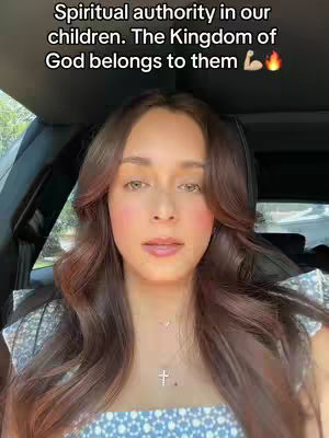 A woman with long brown hair is framed in a selfie-style shot sitting inside a vehicle, with the background softly blurred. The text overlay at the top states: `Spiritual authority in our children. The Kingdom of God belongs to them` accompanied by flexed bicep and fire emojis.