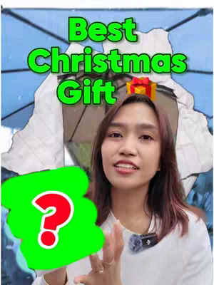 A cover image features a woman smiling and talking to the camera. Overlayed on the image is text saying "Best Christmas Gift" in large green letters. A green shape with a red question mark is in the bottom left corner. Behind the woman's head, a blurred background shows a light-blue sky and a large, open umbrella.