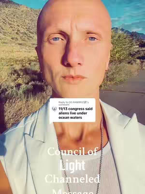 A selfie of a bald man centered in the frame, looking directly at the camera. He has fair skin, blue eyes, and a neutral expression. He is wearing a white vest over a white undershirt and a silver chain necklace. Behind him is a blurred natural environment with some vegetation and what appears to be a road. A white box with a comment appears in front of his chest.