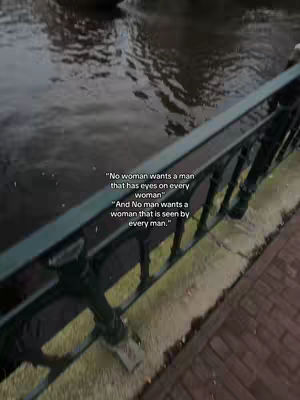 The photo shows a narrow canal scene with a dark water surface under an overcast sky. A black metal railing is in the foreground with text against the dark water background.