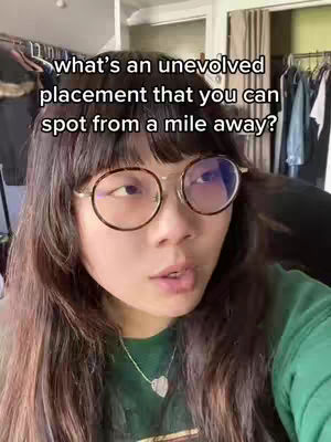 A medium shot of a young woman with long dark hair, wearing round spectacles and a green top, looking at the camera. Text overlayed in white reads: what's an evolved placement that you can spot from a mile away?