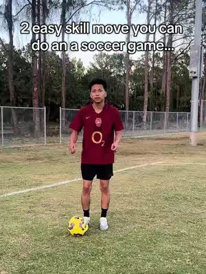 A young man in a maroon soccer jersey stands on a grassy field with a soccer ball at his feet. The background includes trees and a chain-link fence. Text overlay indicates the video is about soccer skills.