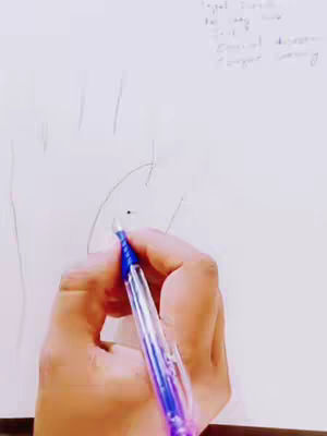 A hand holding a blue pen and drawing on a white piece of paper. In the background, some handwritten text is visible, likely notes related to palmistry.