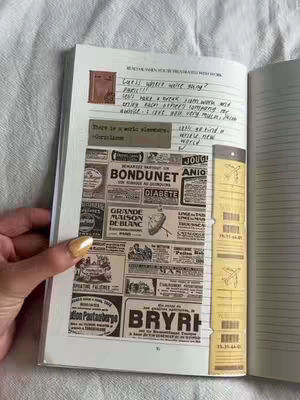 The cover image shows an open journal lying on a white surface, likely a bed. The journal's pages are visible, with handwriting and various layered elements. The left page features a collage of vintage advertisements, adding a textured, aged aesthetic with sepia colors. A hand, with painted nails, enters from the left, pointing at the page. The right page has vertical lines. The overall composition is simple with a focus on visual content.