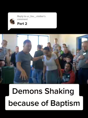 A group of people are in a room, with a man in a grey t-shirt and another person, who is seemingly having a reaction to a religious moment with many people watching.