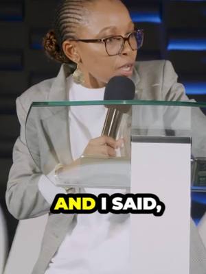 A woman wearing glasses and a blazer stands behind a clear podium with a microphone, speaking. Text overlay in a yellow and black box says, 'AND I SAID,'
