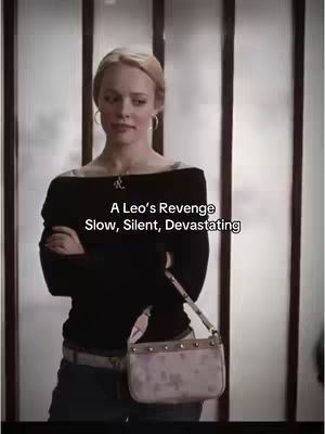 The image features a woman with blonde hair standing in front of a frosted glass background. She is wearing a black off-the-shoulder top, and a small designer purse hangs from her shoulder. Overlayed text at the bottom reads A Leo's Revenge Slow, Silent, Devastating.