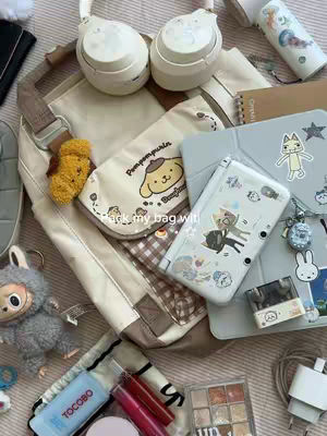 A top-down shot showcases the contents of an open bag with a white background. Items include a pair of white headphones, a small notebook, a light gray case with a game console decorated with stickers, small pouches and bags decorated with cartoon characters and plaid patterns, and a variety of other trinkets. The overall aesthetic of the image is bright and organized, with soft colors and various textures being highlighted due to the overhead lighting.