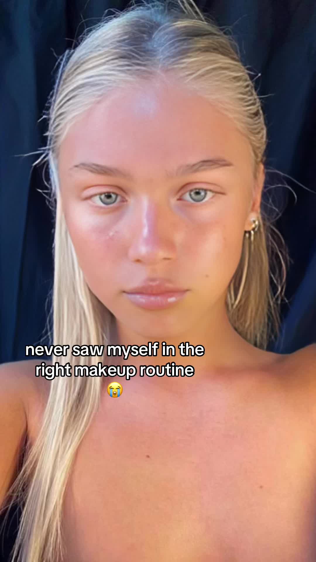 The cover image is a close-up selfie of a fair-skinned woman with blonde hair and blue eyes. She gazes directly at the camera with a neutral expression. The lighting is soft, highlighting her features. The background is dark, which contrasts with her fair skin. The text overlay reads 'never saw myself in the right makeup routine' in a white, bold font.