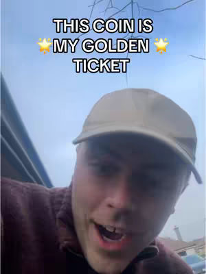 The cover image shows a young man looking towards the camera with an open mouth and a surprised expression. He is wearing a light beige cap and a dark burgundy zip-up jacket. The background is a cloudy sky with the tops of some trees visible. Text overlayed on the image reads: "THIS COIN IS MY GOLDEN TICKET" written in a bold white font with yellow star emojis on either side of the text.
