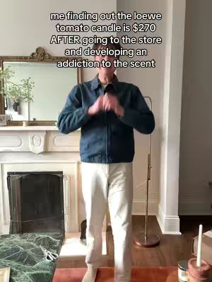A man stands in front of a fireplace, looking surprised. The image has text overlay informing the viewer about the cost of a Loewe candle. The setting appears to be a well-lit home.